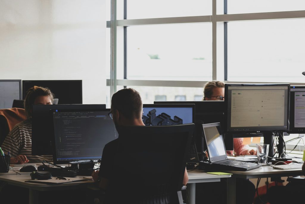 IT team working in a modern office with multiple monitors displaying code and analytics dashboards, collaborative software development environment